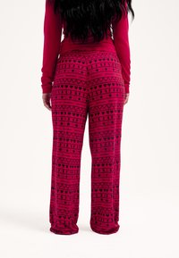 Rózsaszín pizsamanadrág laza szabással, fekete mintával, amelyben szívek, csillagok és sziluettek ismétlődnek. Puha, rugalmas anyagból készült.