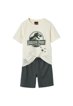 Cremefarbenes Jurassic Park T-Shirt mit Dinosaurier-Logo und Fußabdrücken, kombiniert mit dunkelgrauen Shorts, vor weißem Hintergrund dargestellt.
