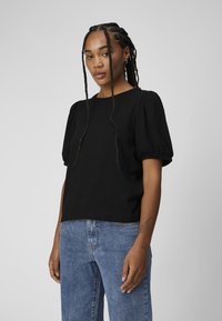 Top noir côtelé avec des manches courtes volumineuses, un col rond et une coupe décontractée, associé à un jean en denim bleu taille haute. Design simple.
