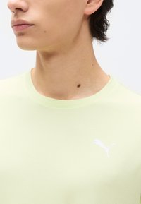 Κοντινό πλάνο ενός ατόμου που φοράει ανοιχτοκίτρινη μπλούζα Puma, δείχνοντας τον λαιμό, μέρος του προσώπου και το λογότυπο Puma στο στήθος.