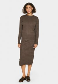 Pull en maille côtelée marron et jupe midi assortie. Présente un col rond, des manches longues et une texture douce. Associé à des mocassins marron.
