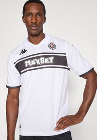 Hvid sportstrøje med en sort stribe og logo, med korte ærmer, krave og teksten "MAXBET" i fed skrift.