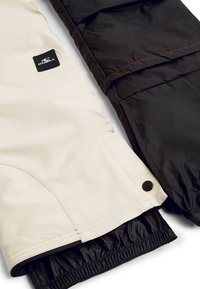 Två jackor sida vid sida: en krämfärgad med en slät textur och logopatch, den andra svart med en matt finish och röda sömmar som accent.
