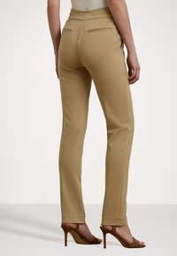 Béžové nohavice s úzkym strihom, hladkou textúrou a dvoma zadnými vreckami, skombinované s hnedými lodičkami na vysokom opätku.
