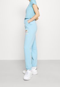 Ljusblå kortärmad t-shirt med grafisk design, matchad med joggers som har broderad blomma och logotyp. Vita sportskor.