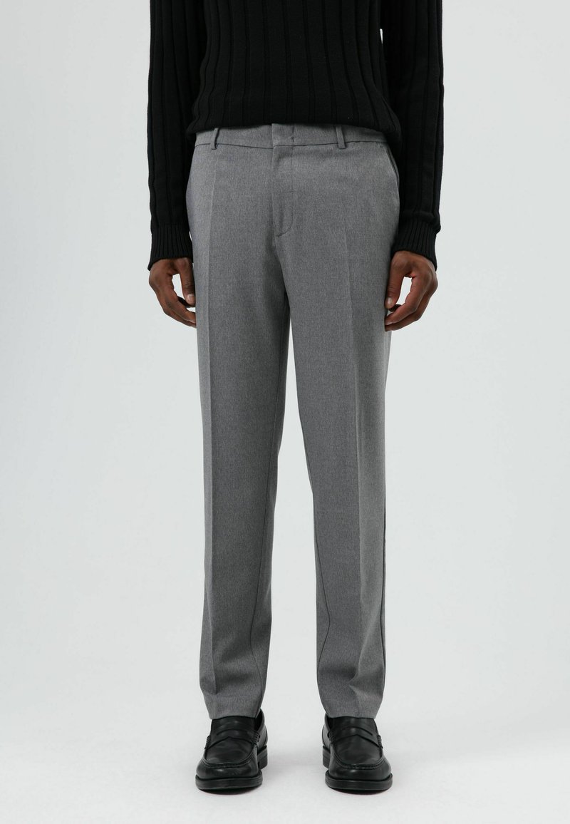 Grijze, op maat gemaakte broek van gestructureerde stof, met een rechte pijp en een voorplooi voor een verzorgde uitstraling. Zwarte schoenen maken het geheel af.