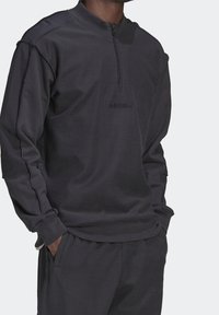 Svart sweatshirt med hög krage och halvdragkedja. Har texturerad tyg, långa ärmar och en broderad logotyp på bröstet.