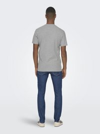 Grijze crew-neck t-shirt en blauwe jeans gezien vanaf de achterkant. Het t-shirt is eenvoudig, en de jeans hebben een lichte taper en zichtbare stiksels.