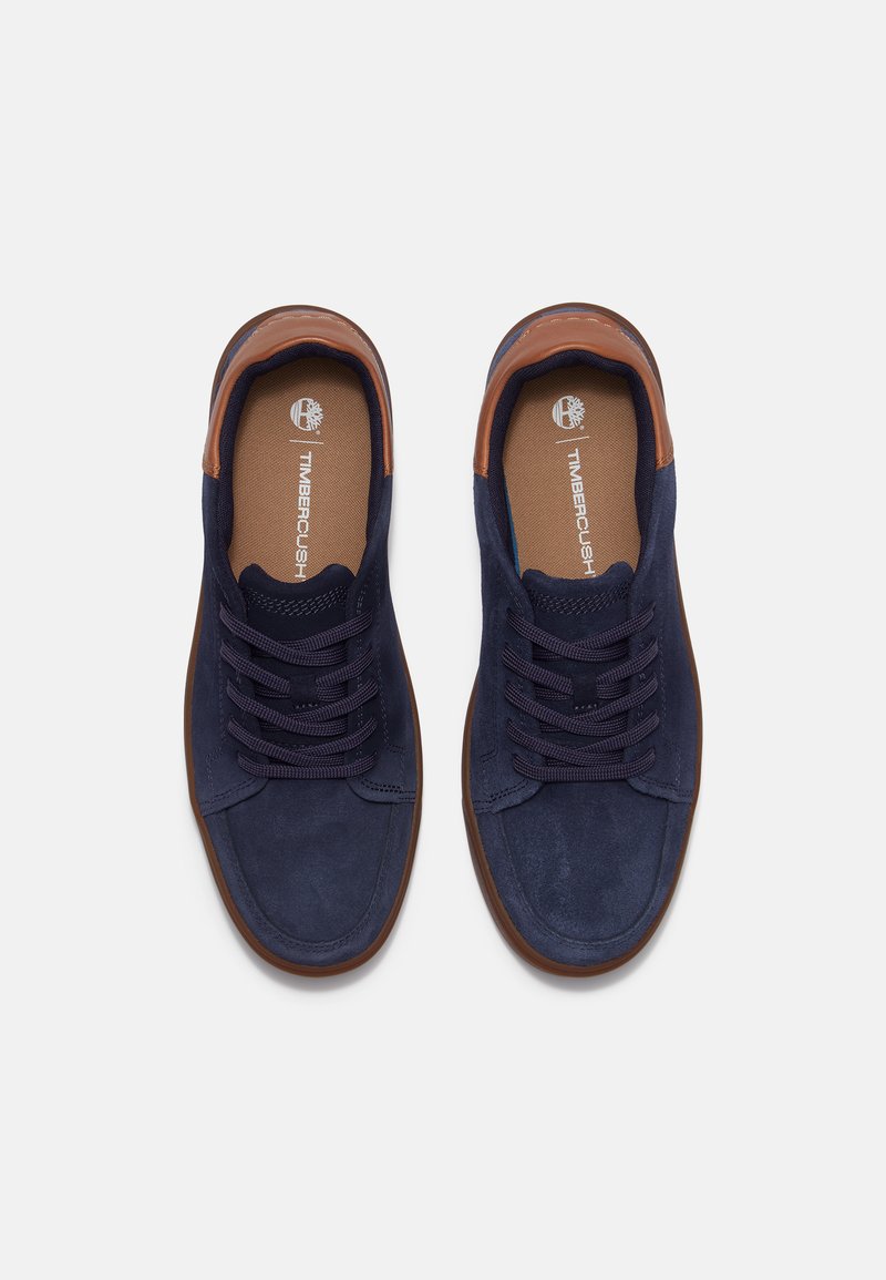 Sneakers in camoscio blu navy con dettagli in pelle marrone, punta rotonda e lacci piatti. Logo Timberland visibile sulla soletta.