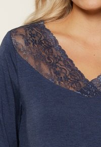 Haut bleu marine avec un décolleté en V profond, présentant des détails en dentelle bleu marine délicats le long du col, texture de tissu douce.