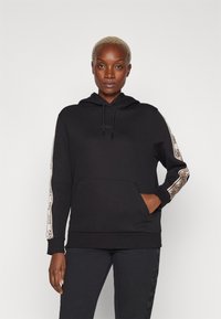 Felpa nera con tasca frontale, polsini elasticizzati e strisce laterali beige a fantasia. Presenta lacci e un logo sul petto.