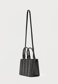 Μαύρη ορθογώνια τσάντα χειρός με υφασμένο σχέδιο ζιγκ-ζαγκ, δύο κοντά χερούλια και ένα ρυθμιζόμενο μακρύ ιμάντα ώμου σε απλό φόντο.