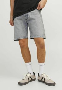 Pantaloncini in denim grigio chiaro con vestibilità ampia, orlo sfrangiato e tasche laterali, abbinati a sneaker beige e calzini bianchi con scritta.