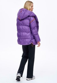 Fialová zateplená bunda s kapucňou, ktorá má oranžové švy a šnúrku na spodnom okraji. Ľahký, lesklý materiál.