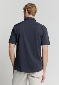 Marineblauwe polo met korte mouwen in een relaxed fit, platte kraag en een gladde textuur; naden zijn netjes gestikt voor een schone afwerking.