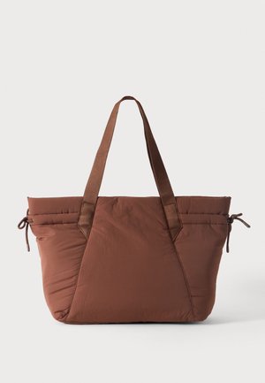 Grand sac cabas marron avec deux longues anses, texture matelassée douce et détails de cordons sur les côtés, sur fond blanc uni.