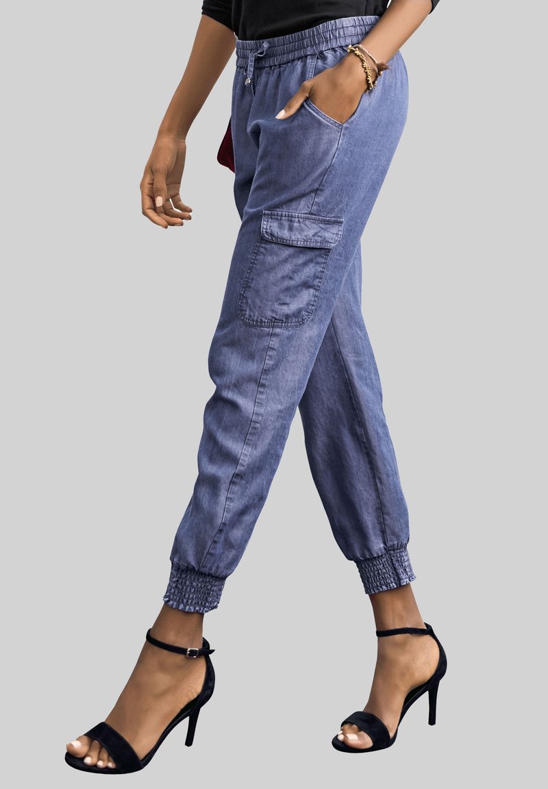 Svijetloplave denim jogger hlače s elastičnim manžetama, bočnim džepovima i kontrastnim šavovima, uparene s crnim sandalama na visoku petu.