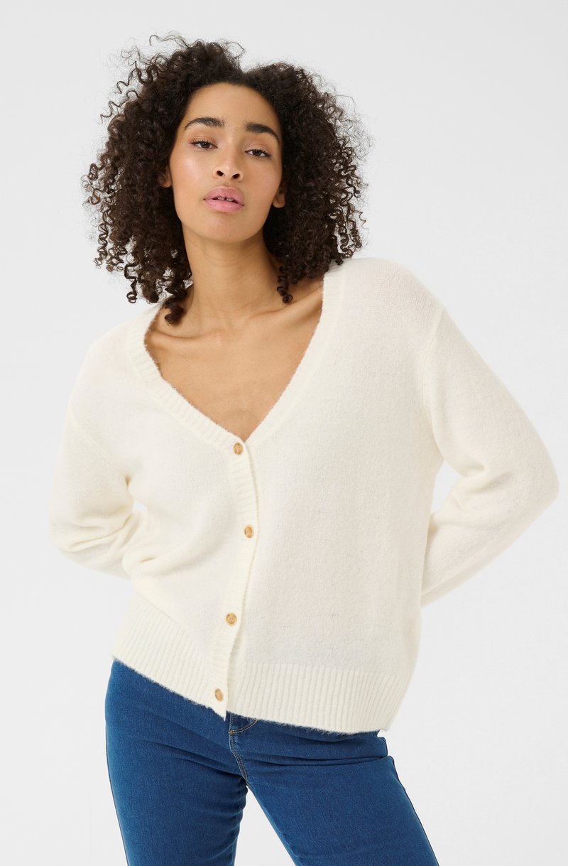Cream-colored cardigan with a deep V-neck, ribbed cuffs, and five wooden buttons down the front. Soft, fuzzy texture, paired with blue jeans.