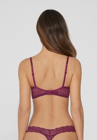 Soutien-gorge en dentelle bordeaux avec des bretelles ajustables, présentant un motif floral et une fermeture à crochets à l'arrière, accompagné d'un string en dentelle assorti.