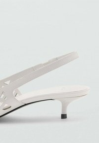 Valkoinen slingback-sandaali, jossa on leikattu geometrinen muotoilu, matala korko ja sileä pinta. Varusteena musta pohjakorostus.