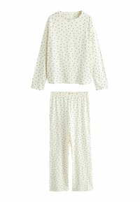 Kreemikas pidžaamasärk ja püksid, mõlemal mustade täppidega hajutatud muster. Pehme kangas ja elastse vöökohaga.