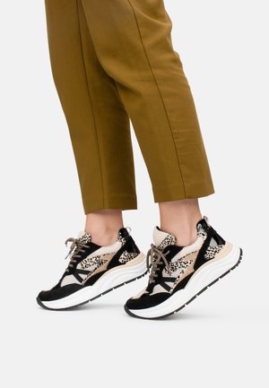 Baskets noires et beige avec un dessus en maille à imprimé léopard, semelle épaisse blanche et lacets contrastés, présentées avec un pantalon olive court.