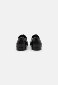 Zapatos de cuero negros con una textura suave, forma redondeada, tacones bajos y un detalle de costura mínimo en la parte de atrás.