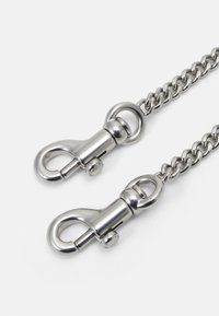 Metalowy łańcuch z dwoma zapięciami typu lobster. Łańcuch charakteryzuje się połączonymi owalnymi ogniwami, a każde z zapięć ma gładkie metaliczne wykończenie.
