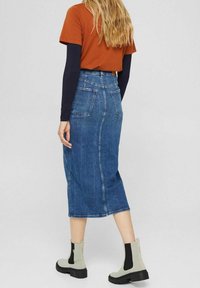 Džínová midi sukně s přiléhavým pasem a dvěma zadními kapsami, kombinovaná s oranžovým topem s krátkým rukávem a šedými kotníkovými botami.