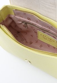 Portafoglio in pelle gialla texturizzata con chiusura a zip, dotato di rivestimento rosa e tasche interne. Etichetta del marchio visibile all'interno.