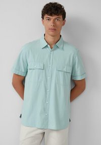 Kurzärmliges Button-Down-Hemd in hellem Minzgrün, mit strukturiertem Stoff, zwei Fronttaschen und einem geraden Saum mit leichter Kurve an den Seiten.