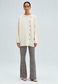 Cream sweater with a round neckline and side buttons, paired with plaid flared pants. Soft texture; buttons are large and light-colored.
