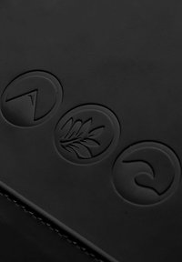 Drei schwarze, geprägte, kreisförmige Tasten auf einer dunklen Oberfläche, jede mit einem markanten abstrakten Symbol: Pfeil, Blatt und geschwungene Form.