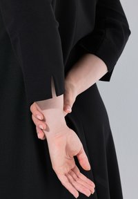 Czarna odzież z rozcięciem rękawa, odsłaniającym rękę trzymającą nadgarstek. Gładka tekstura materiału; minimalistyczny design.