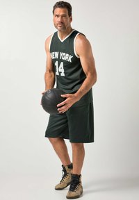 Camiseta de baloncesto verde oscuro con "NEW YORK" y número "14" en blanco, combinada con pantalones cortos a juego. Balón de baloncesto negro sostenido en las manos, zapatillas marrón claro usadas.