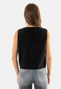 Top negro sin mangas con escote redondeado y corte relajado, combinado con jeans ajustados de color gris claro que cuentan con bolsillos traseros.