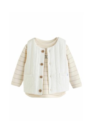 Vit texturerad väst med bruna knappar över en kräm- och beige-randig långärmad skjorta med grafiskt tryck.