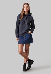 Tmavosivá mikina s predným vreckom a šnúrkami, skombinovaná s džínsovou mini sukňou. Čierne šnurovacie topánky a ponožky dopĺňajú outfit.