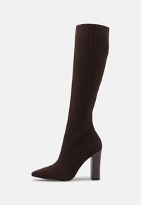 Bottes marron hauteur genou avec un design côtelé, un bout pointu et un talon épais. Fabriquées en tissu extensible pour un ajustement serré.