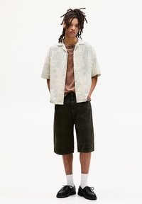 Kortærmetternet skjorte i crem, brunt T-shirt under, mørkegrønne shorts, sorte sko og hvide sokker. Enkle smykke detaljer.