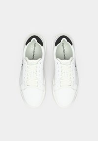 Witte Calvin Klein Jeans sneakers met zwart hieldetail, witte veters en zichtbaar merklogo binnenin de schoen, zichtbaar van bovenaf.