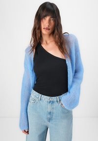 Lichtblauwe mohair cardigan met lange mouwen over een zwarte geribde tanktop, gecombineerd met lichtblauwe jeans met een hoge taille. Geen zichtbare patronen.