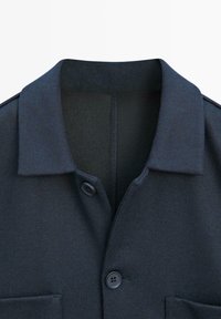 Colletto di camicia blu navy scuro con due bottoni allacciati e cuciture superiori visibili, su sfondo bianco semplice.