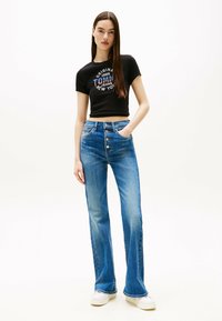 Przycięta czarna koszulka z grafiką "Tommy Jeans New York", połączona z niebieskimi jeansami z wysokim stanem w kształcie dzwonów, posiadającymi pięć guzików i kieszenie z przodu.