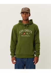 Felpa con cappuccio verde oliva, dotata di tasca frontale a marsupio, cappuccio con cordino e logo bianco "LES DEUX". Abbinata a jeans in denim.