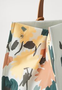 Sac fourre-tout à motifs floraux avec des accents jaunes, pêches et verts. Dispose d'un fermoir à snap en or et d'un intérieur en tissu doux. Bretelles marron.