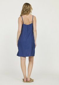 Robe bleue sans manches avec une coupe droite, une texture transparente et une fermeture à boutons au dos. L'ourlet tombe juste au-dessus du genou.