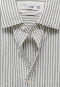 Camicia a righe grigio chiaro e bianco con bottoni, colletto ampio, tessuto strutturato e bottoni in plastica trasparente.
