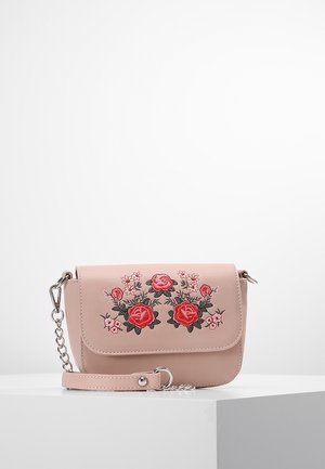 Lille lyserød taske med rød og pink blomsterbroderi og en sølvkæde, placeret på en hvid piedestal mod en hvid baggrund.