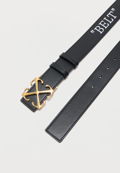Μαύρη δερμάτινη ζώνη με χρυσή αγκράφα σε σχήμα Χ και λευκό κείμενο «BELT» τυπωμένο κοντά στο τέλος σε απλό φόντο.